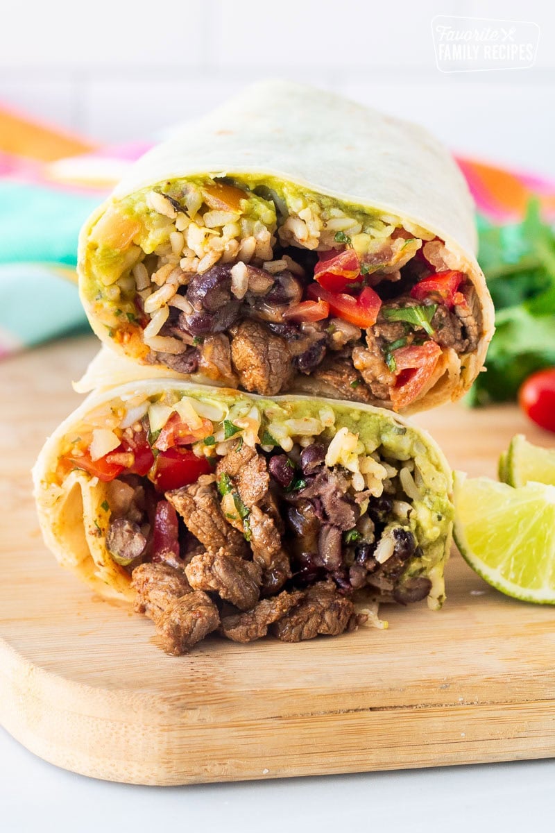 Cut in half Carne Asada burrito stacked on top of each other, filled with guacamole, pico de gallo, cilantro lime rice, black beans, shredded cheese and cut Carne Asada.