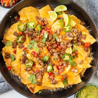 Carne Asada nachos with toppings including sliced jalapeños, pico de gallo, cilantro, and lime wedges.