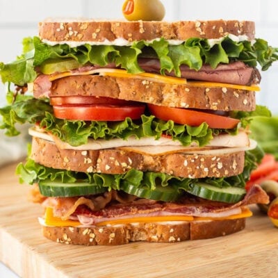 Large Dagwood sandwich with toasted bread, cheddar cheese, ham, bacon, turkey breast, lettuce, tomatoes, cheese, roast beef, pickle and mayo.