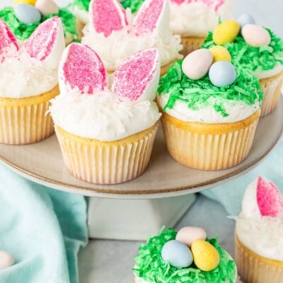 Easter Cupcakes on a cake stand shaped like bunnies and nests with chocolate Cadbury eggs.
