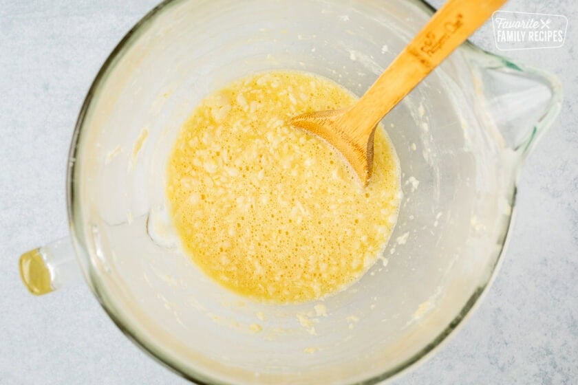 Mixing bowl with butter, sugar and eggs combined with a wooden spoon.