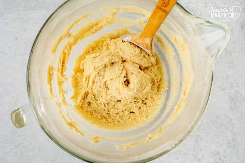 Italian lemon cookie dough in a glass mixing bowl with a wooden spoon.