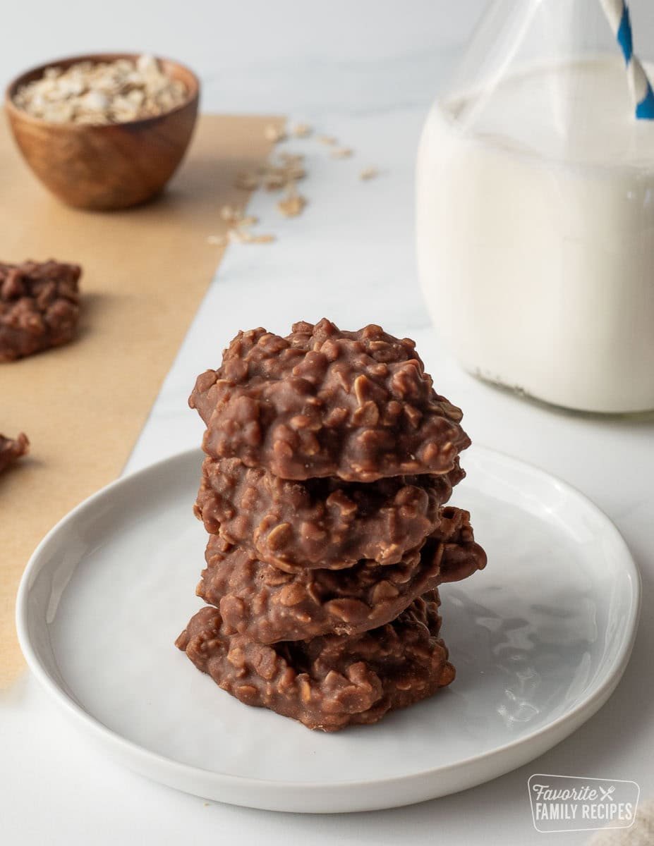 A stack of four no bake cookies stacked on a plate with a pitcher of milk in the background.