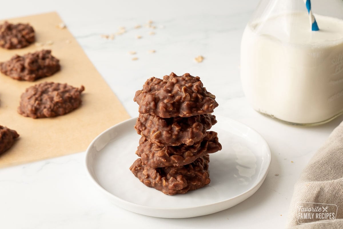 Four chocolate and peanut butter no bake cookies stacked next to a jar of milk