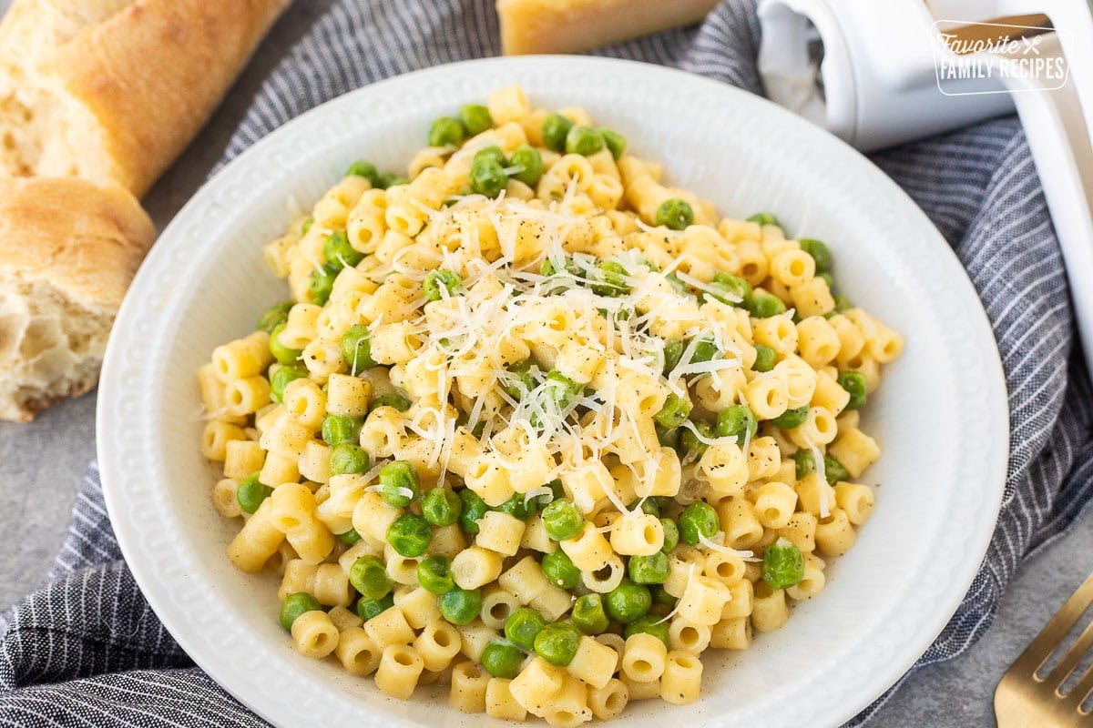 Pasta with peas in a small bowl with fresh grated cheese and pepper.
