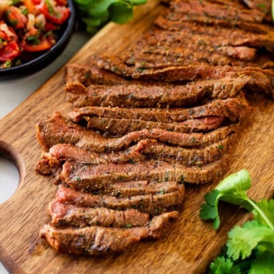 Grilled Carne Asada sliced on a cutting board. Pico de Gallo on the side.