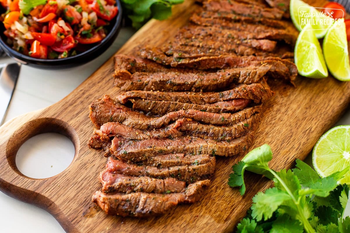 Grilled Carne Asada sliced on a cutting board. Pico de Gallo on the side.