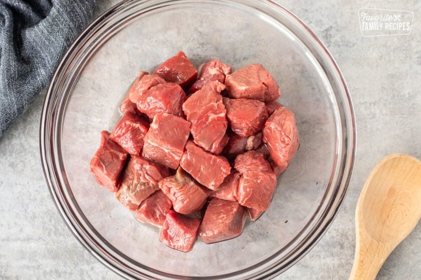 Glass mixing bowl with cut up steak and oil mixed together.