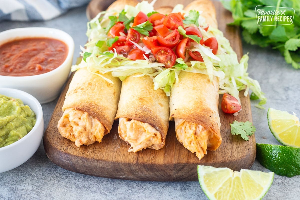 Three chicken flautas lined up together with shredded lettuce, chopped tomatoes and cilantro on top.