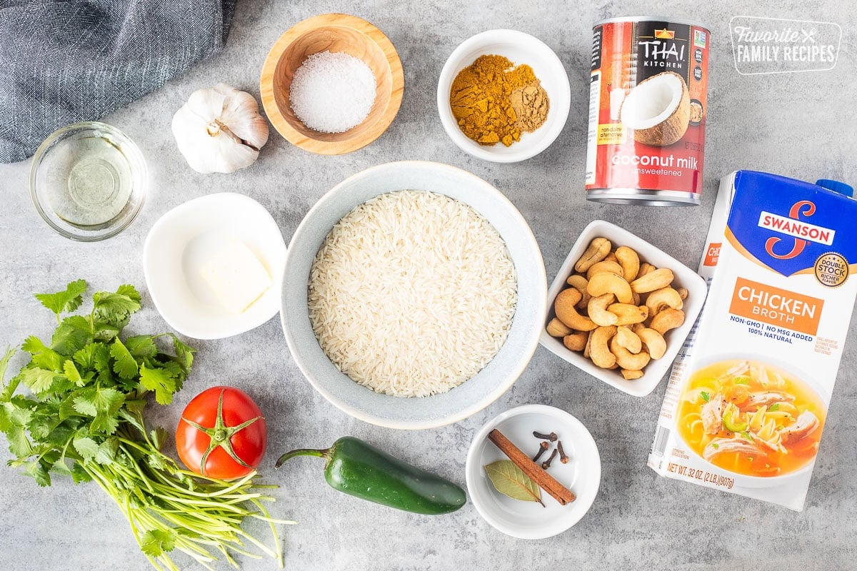 Ingredients to make coconut rice including rice, cashews, seasonings, coconut milk, chicken broth, jalapeño, tomato, cilantro, butter, garlic, salt and oil.