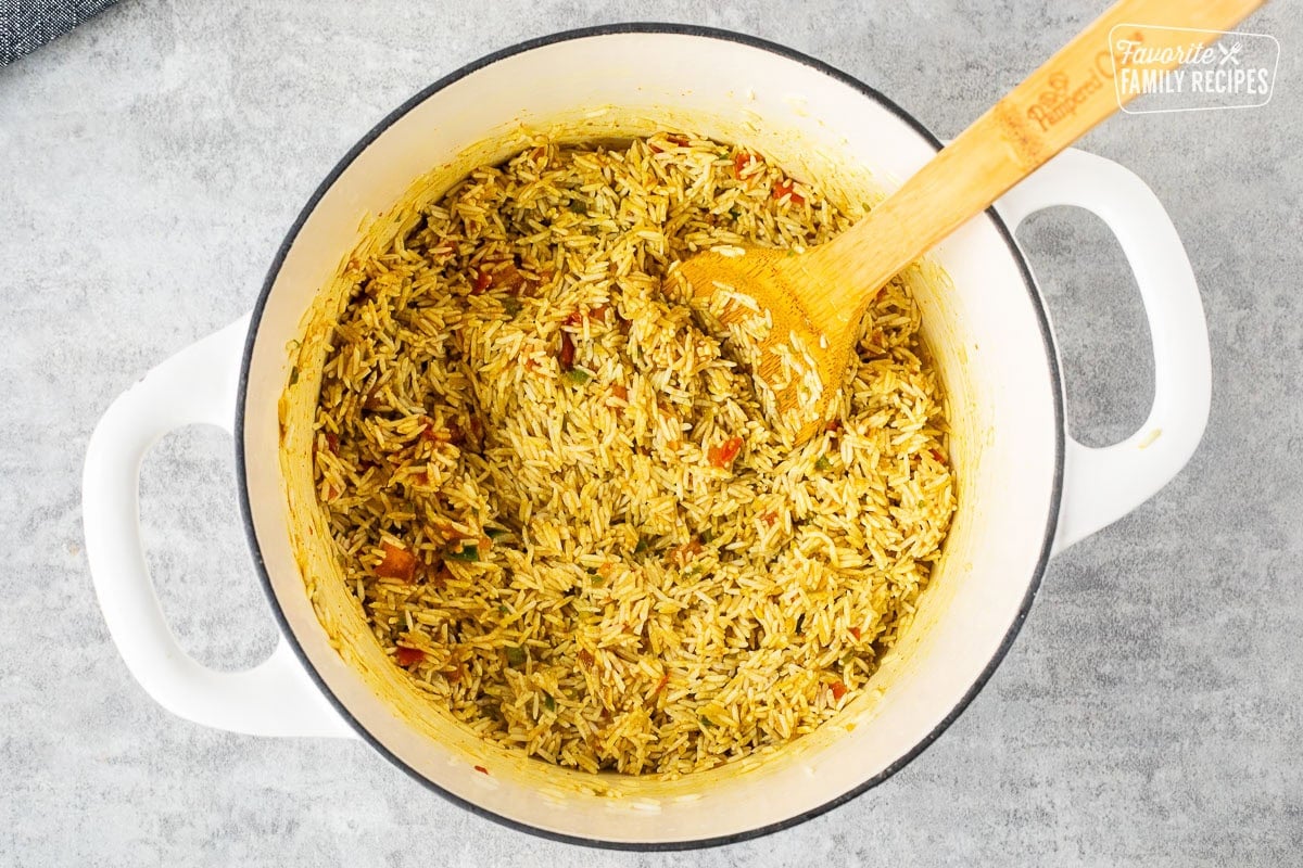 Skillet of rice combined with seasonings and a wooden spoon.