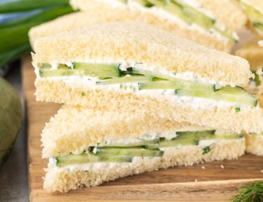 Cut cucumber sandwiches on a cutting board stacked on top of each other.