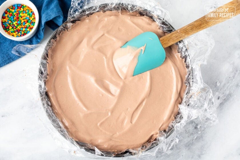 Spreading chocolate ice cream into a springform pan lined with plastic wrap and spatula.