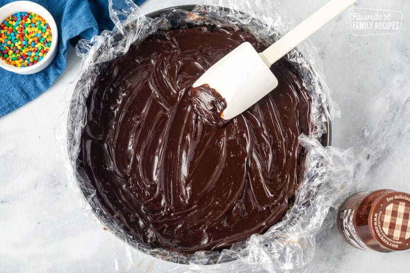 Spreading hot fudge in a springform pan lined with plastic wrap and spatula.