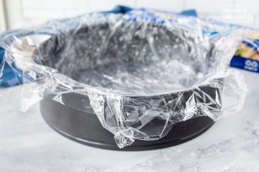 Springform pan with layers of plastic wrap on top.