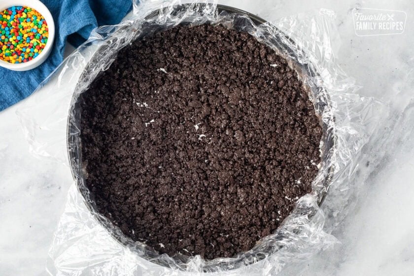 Oreo mixture layer in a springform pan lined with plastic wrap.