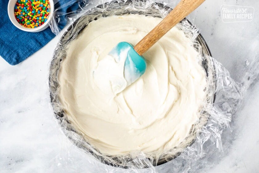 Spreading vanilla ice cream into a springform pan lined with plastic wrap and spatula.
