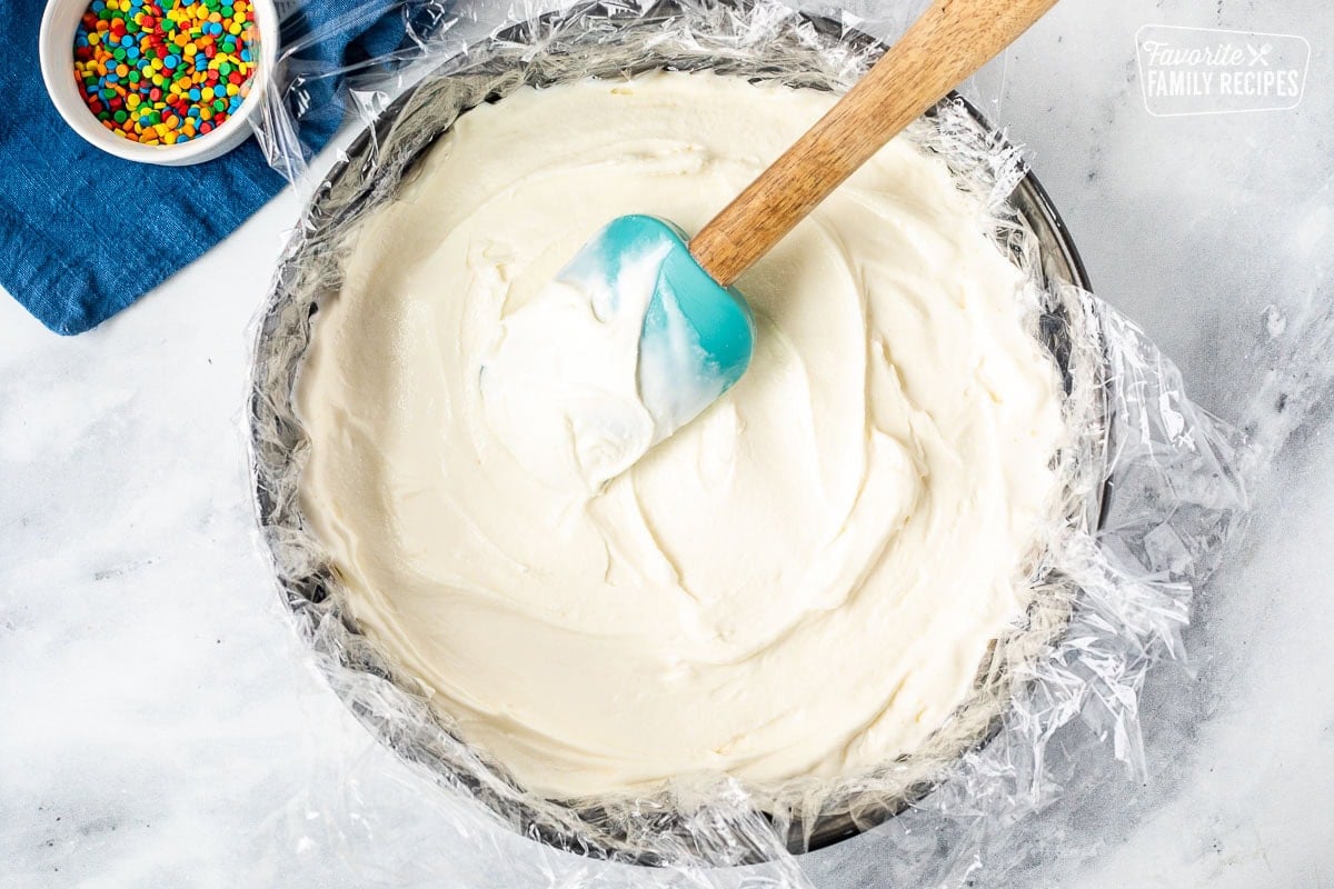 Spreading vanilla ice cream into a springform pan lined with plastic wrap and spatula.