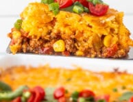 Spatula holding a slice of Mexican cornbread casserole topped with fresh cilantro, diced tomatoes and jalapeños.