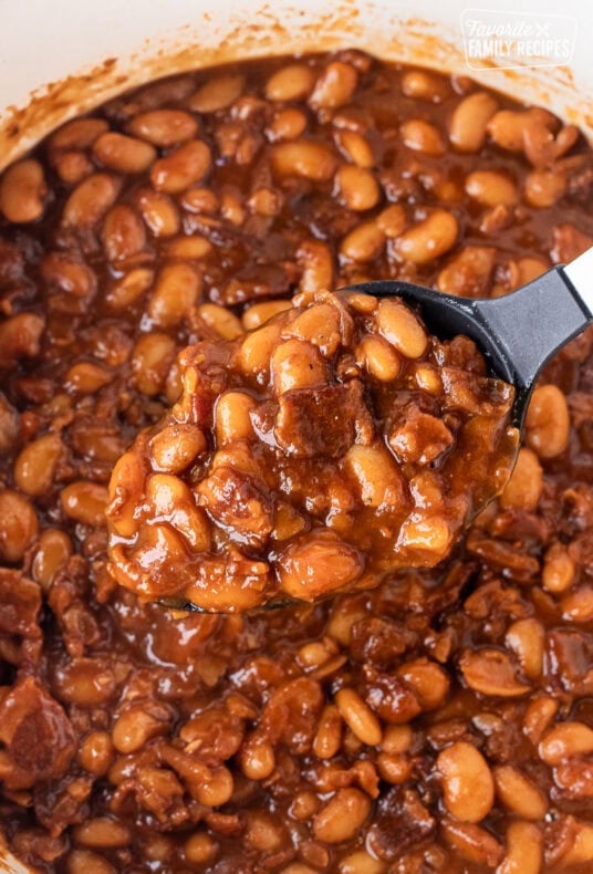 Spoon holding a scoop of pork and beans over a Dutch oven.
