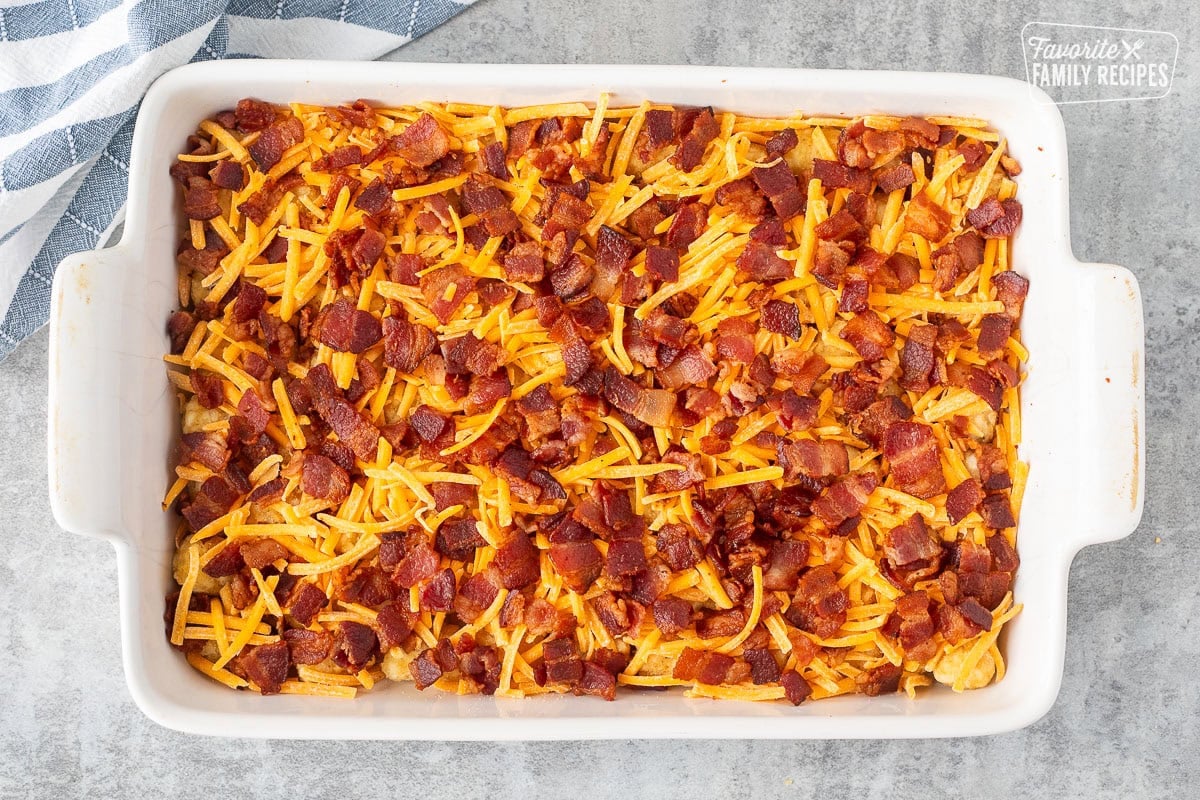 Baking dish with frozen tater tots, shredded cheddar cheese and cut up crispy bacon.