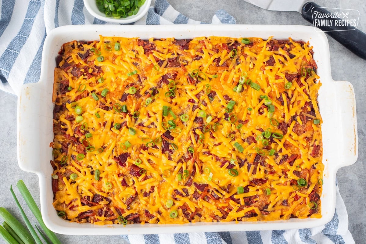 Baking dish of Tater tot breakfast casserole with tater tots, cheddar cheese, bacon and garnished with green onions.
