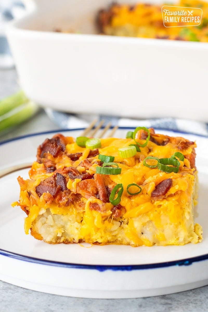 Slice of tater tot breakfast casserole with tater tots, cheddar cheese, bacon and garnished with green onions.