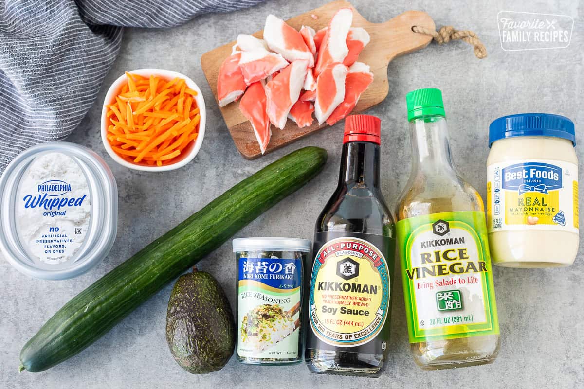 Ingredients to make California Roll Cucumber Salad including an English cucumber, soy sauce, mayo, rice vinegar, crab, carrots, whipped cream cheese, avocado and nori furikake.