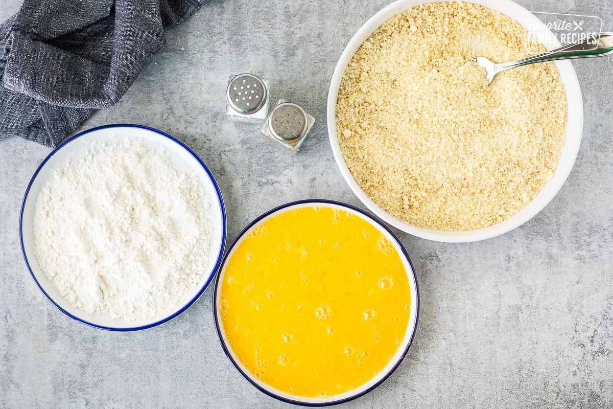 Plate of flour, plate of egg wash and bowl of bread crumbs with a fork.