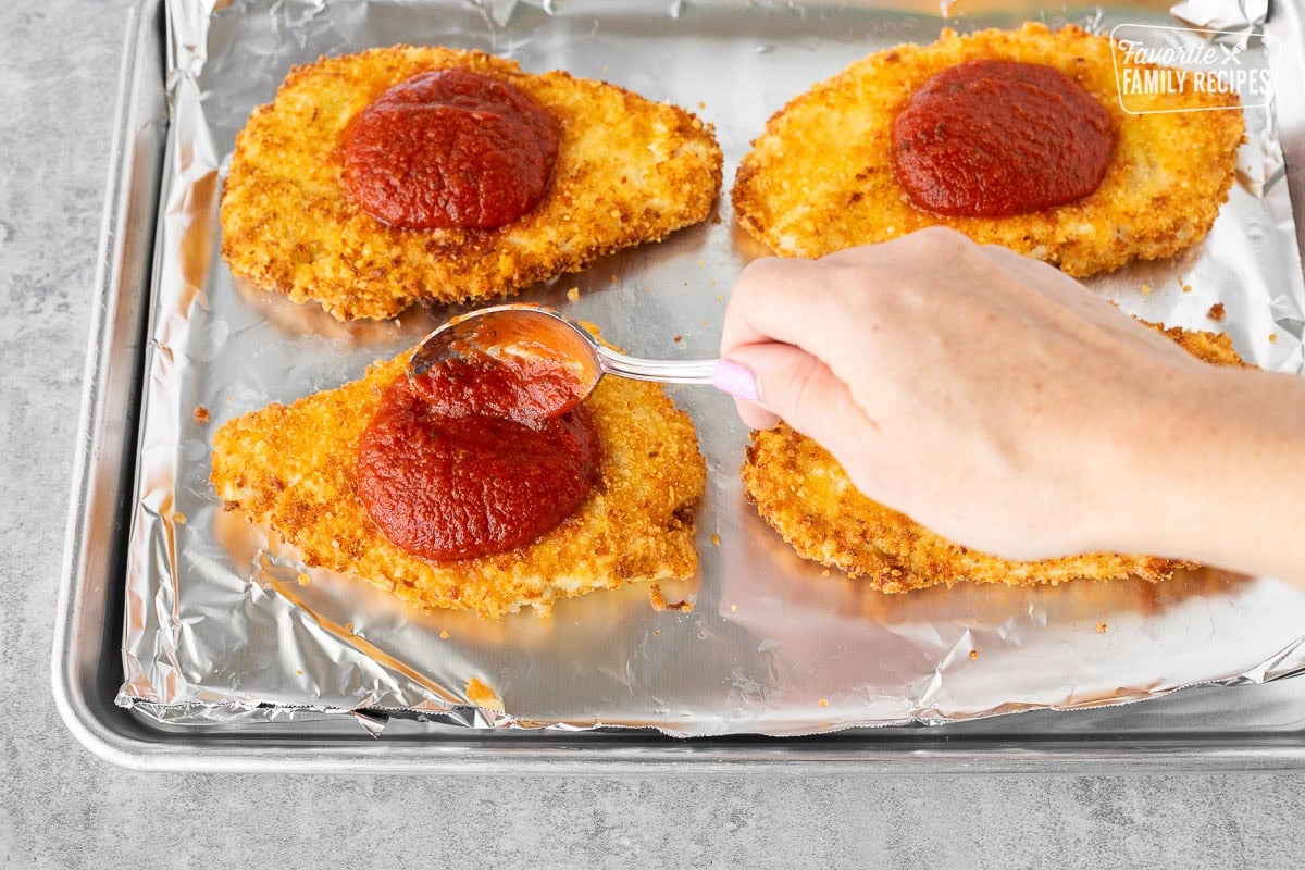 Spooning marinara onto fried chicken breasts.