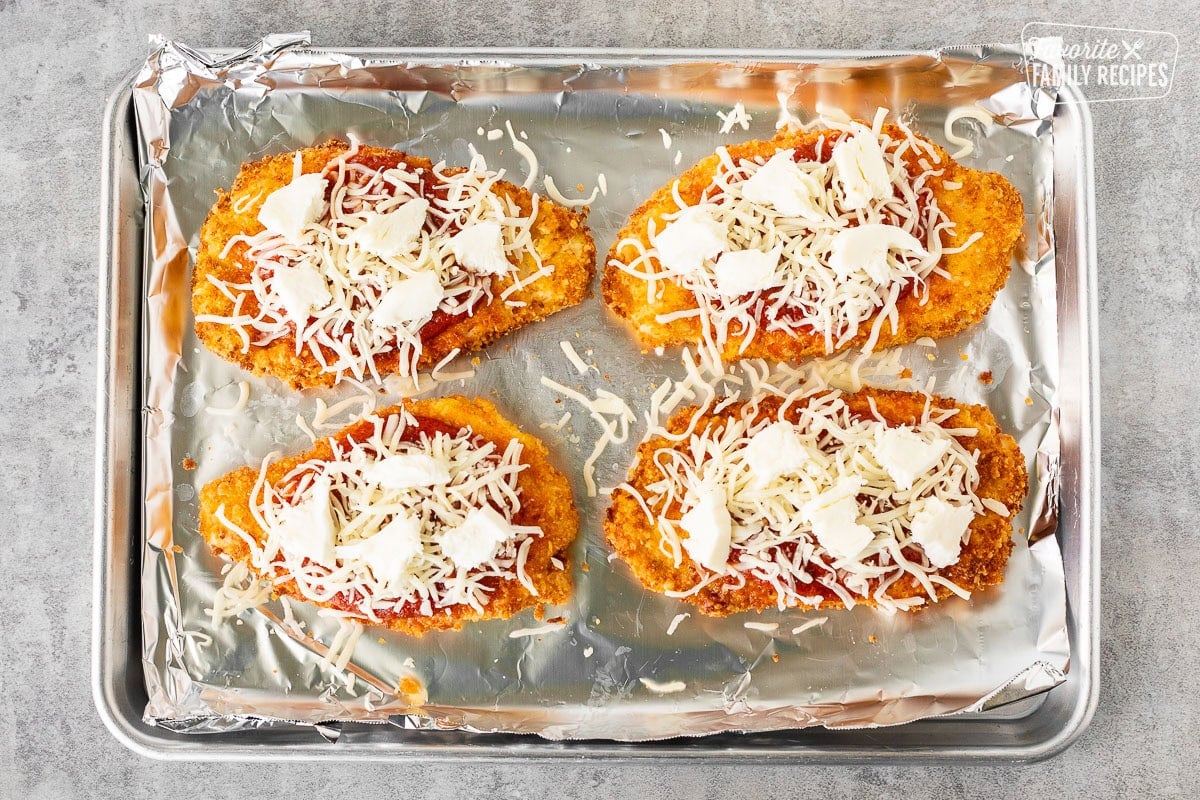 Sprinkling cheese on top of Chicken Parmesan with marinara.