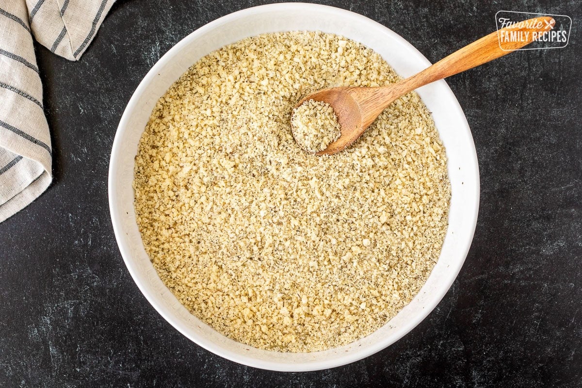 Glass bowl with panko crumb mixture and a wooden spoon.