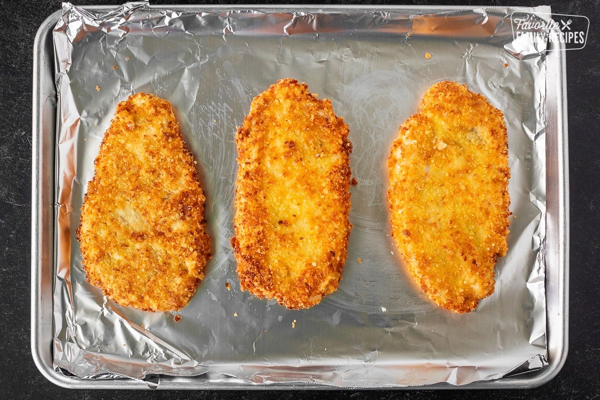 Three fried breaded chicken breast on a baking sheet lined with foil.