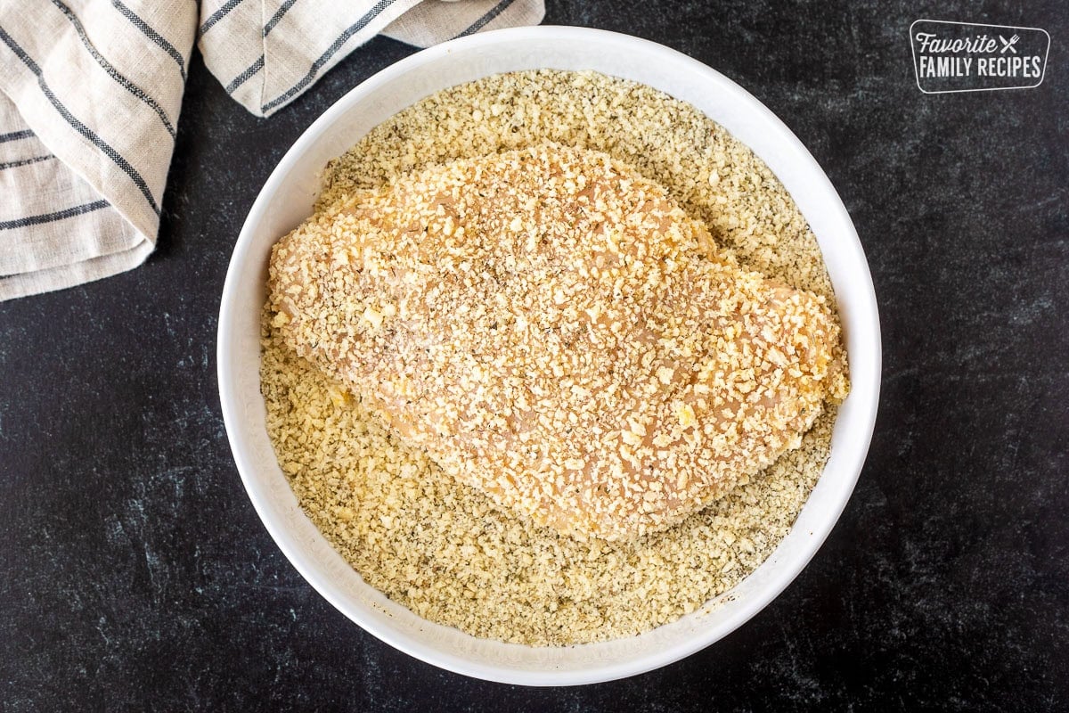 Chicken breast dipped into bowl of panko bread crumb mixture.