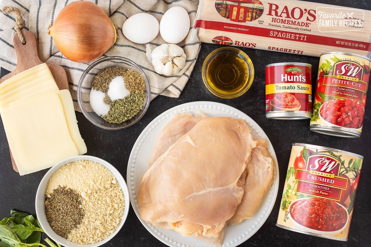 Ingredients to make Chicken Parmesan including spaghetti pasta, chicken breasts, crushed tomatoes, diced tomatoes, tomato sauce, garlic, eggs, onion, spices, panko bread crumbs, Parmesan cheese, basil and mozzarella slices.