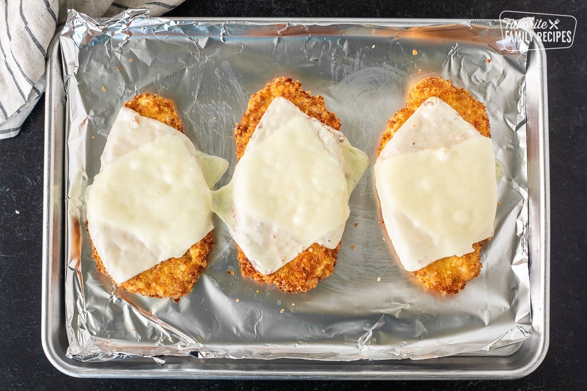 Three breaded and fried chicken breasts with melted slices of mozzarella cheese on top.