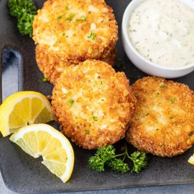 Crab cakes on a plate with a small bowl of tartar sauce.