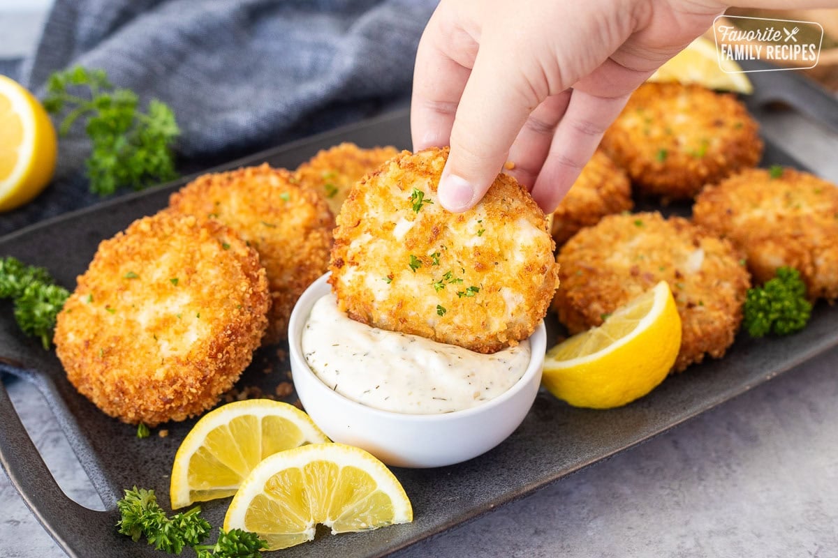 Dipping a crab cake into a small bowl of tartar sauce.