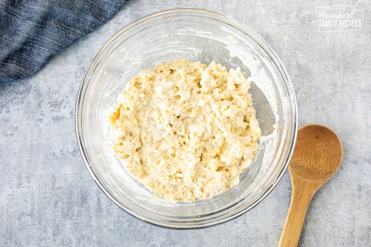 Glass mixing bowl with crab cake mixture and a wooden spoon on the side.