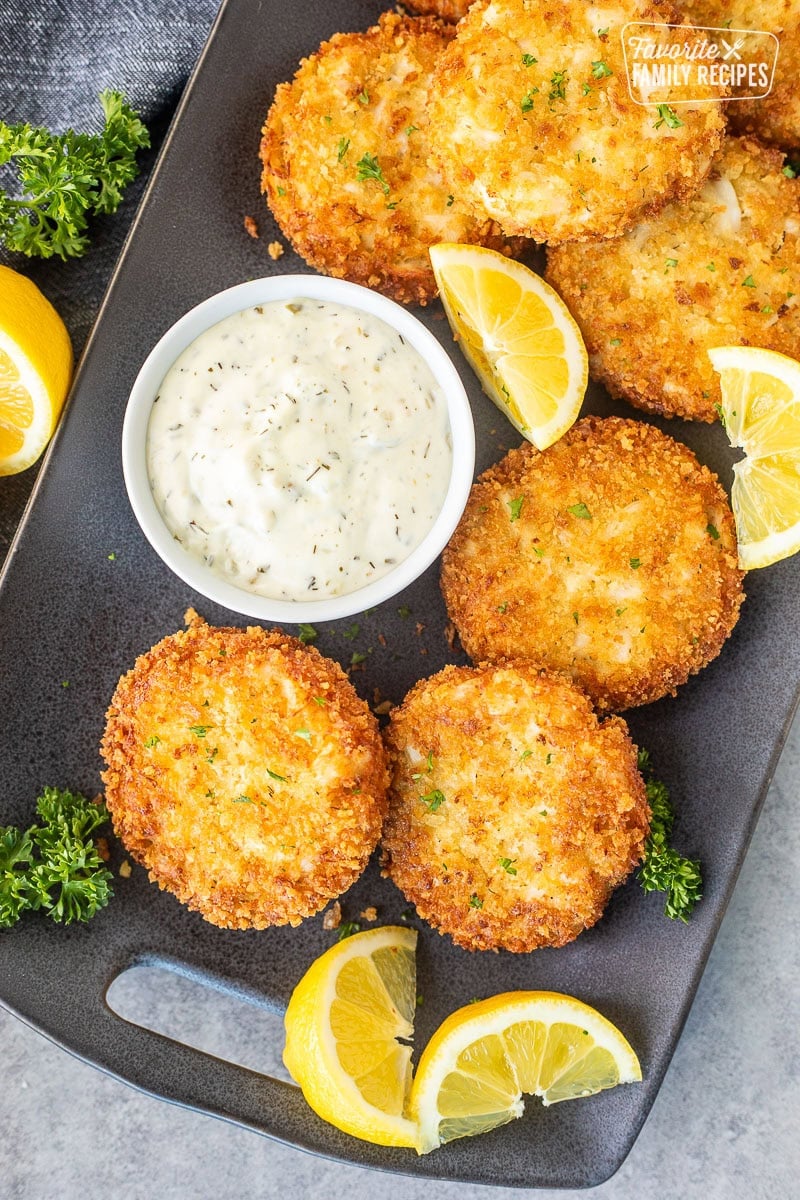 Golden crab cakes on a platter with a small bowl of tartar sauce.
