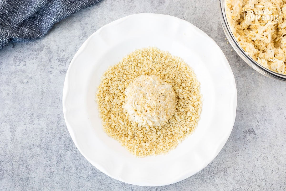 Glass bowl with crab cake mixture shaped in a round and dipped in panko bread crumbs.