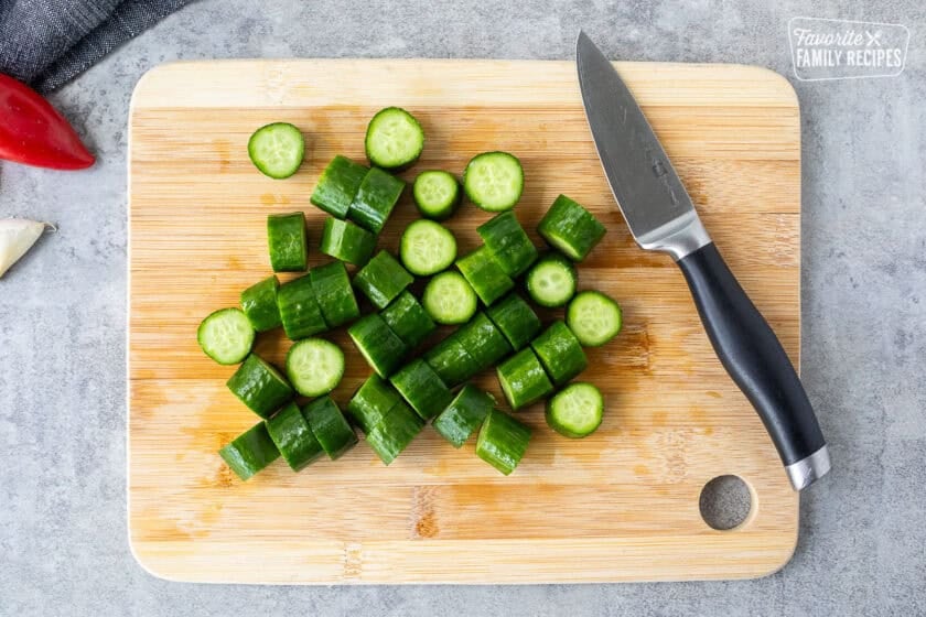 Chopped baby cucumbers on a cutting board with a knife.