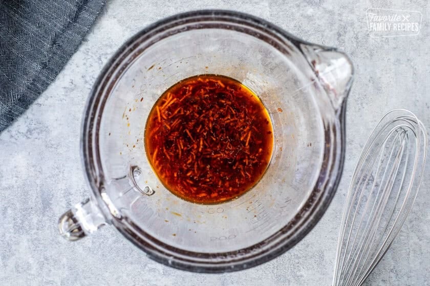Glass bowl with marinade with a whisk on the side.