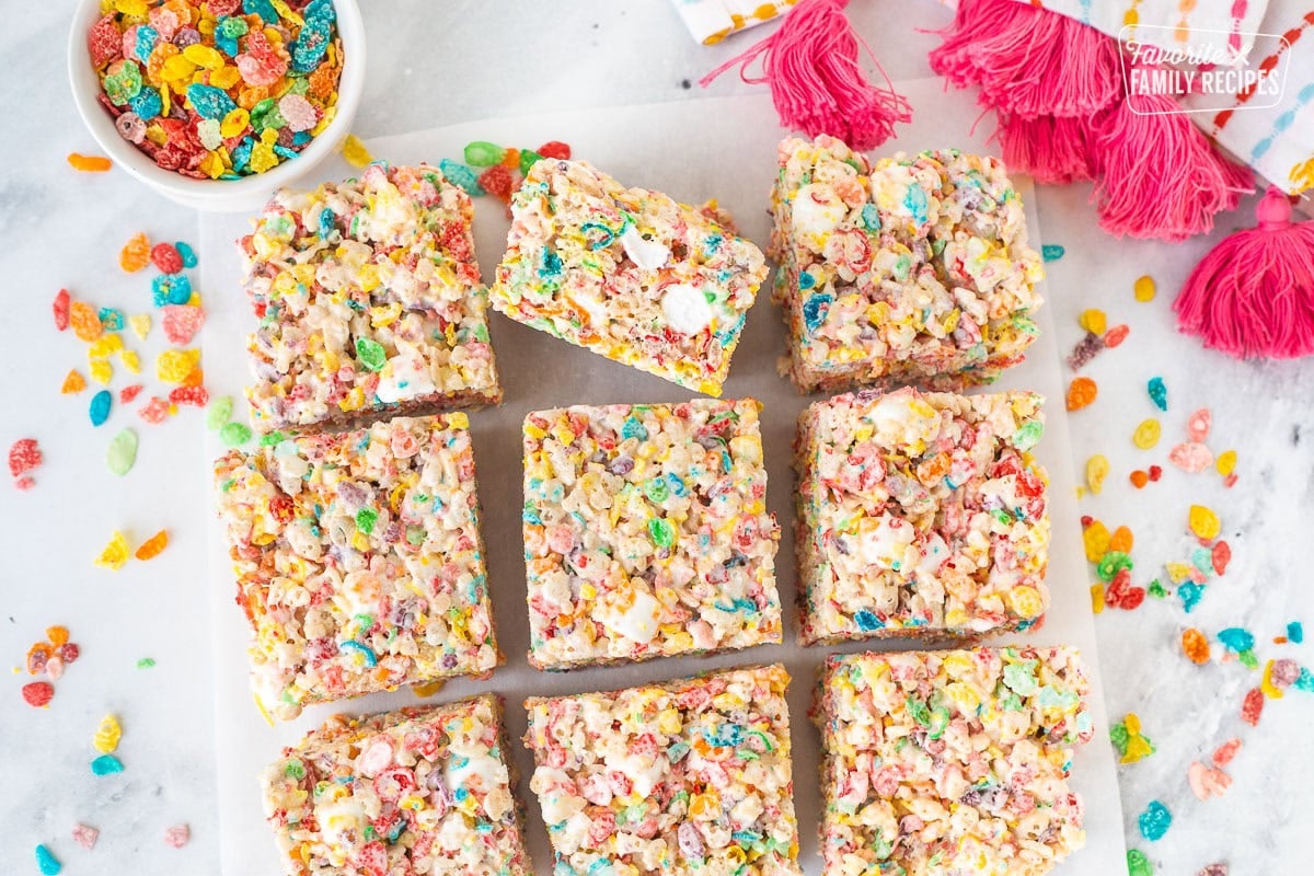 Fruity pebbles rice crispy treats cut into nine squares on parchment paper.