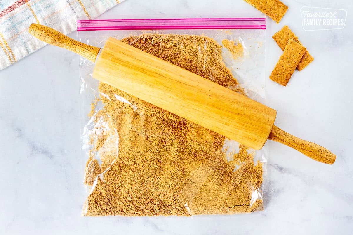 Plastic bag with crushed graham crackers and a rolling pin on top.