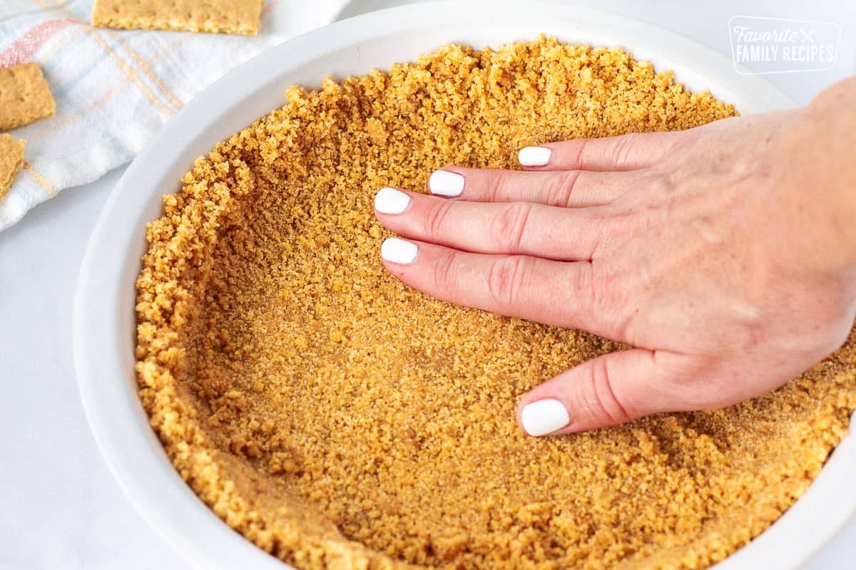 Pressing down graham cracker pie crust by hand into a pie plate.