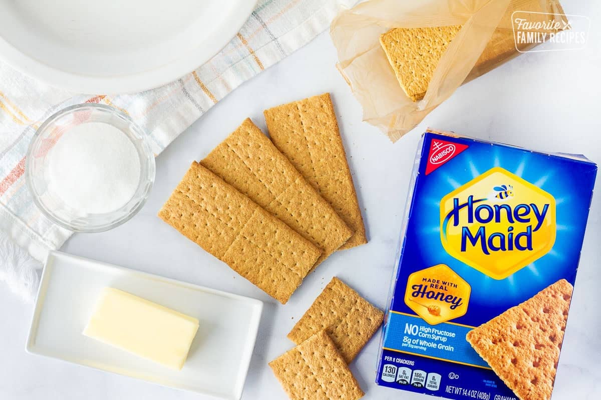 Ingredients to make graham cracker pie crust including graham crackers, butter, and sugar.