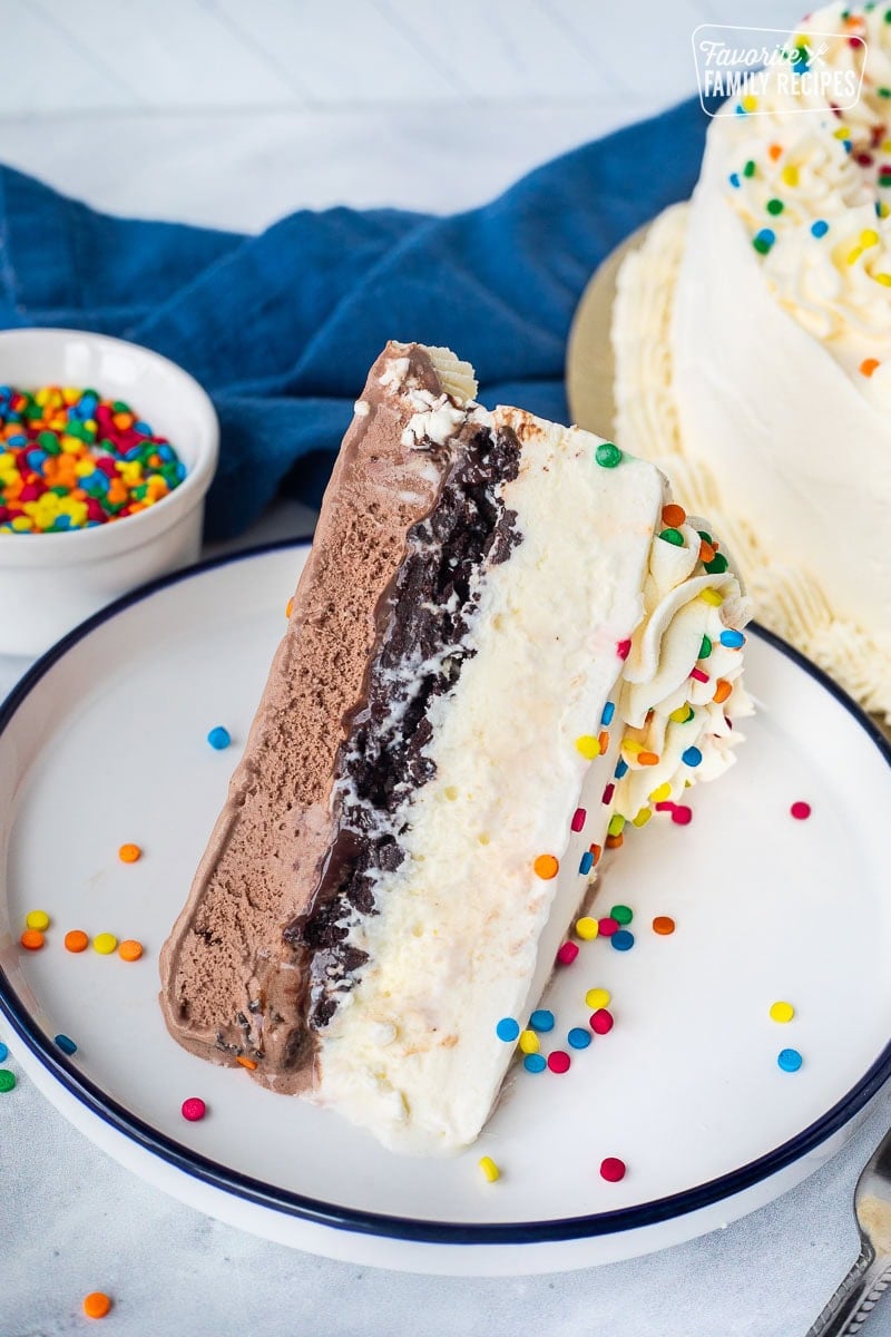 Slice of Ice Cream cake with layers of whipped cream, vanilla ice cream, Oreo, fudge and chocolate ice cream.