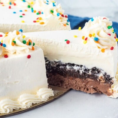 Pulling out a slice of Ice cream cake with layers of Slice of Ice Cream cake with layers of whipped cream, vanilla ice cream, Oreo, fudge and chocolate ice cream.