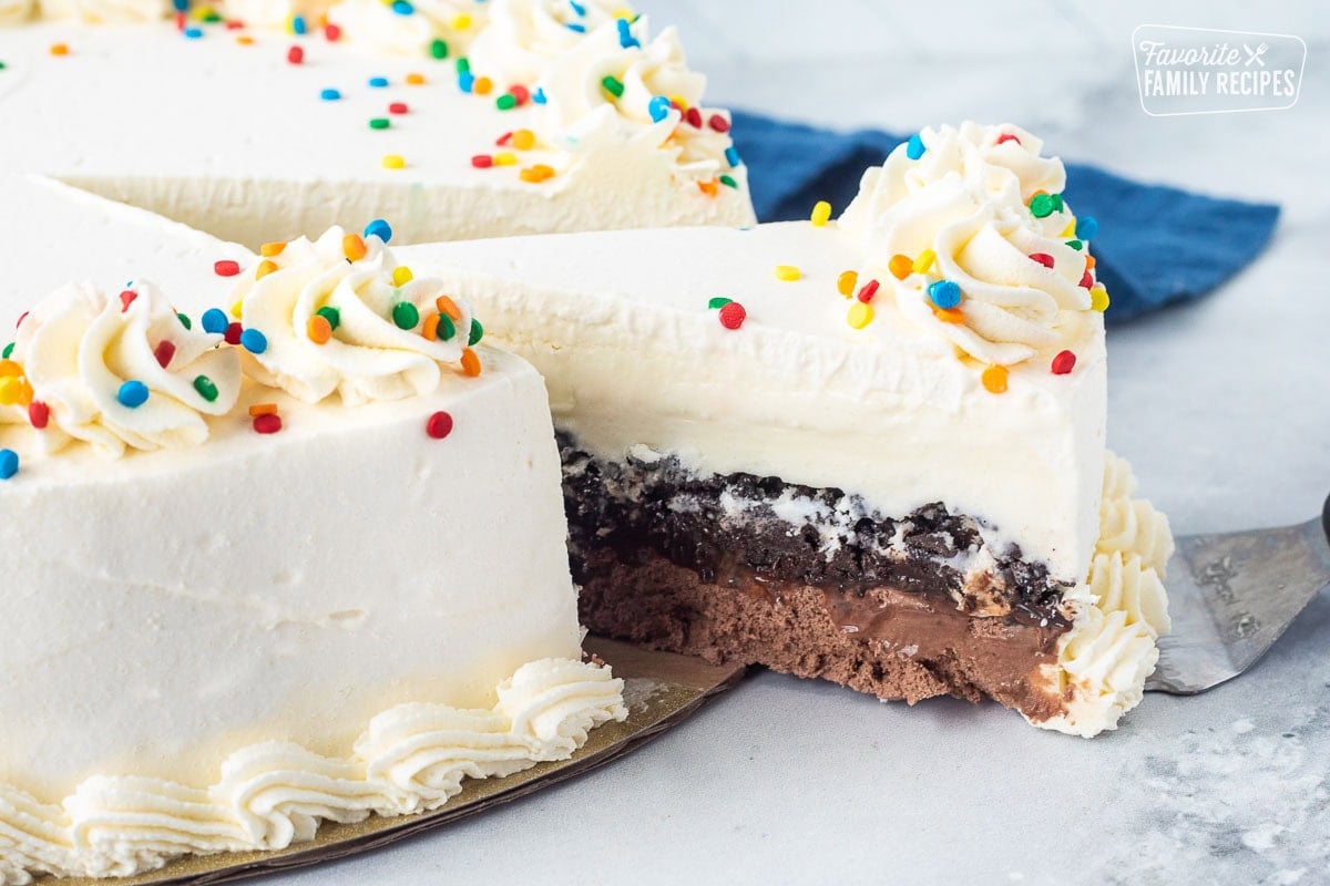 Pulling out a slice of Ice cream cake with layers of Slice of Ice Cream cake with layers of whipped cream, vanilla ice cream, Oreo, fudge and chocolate ice cream.